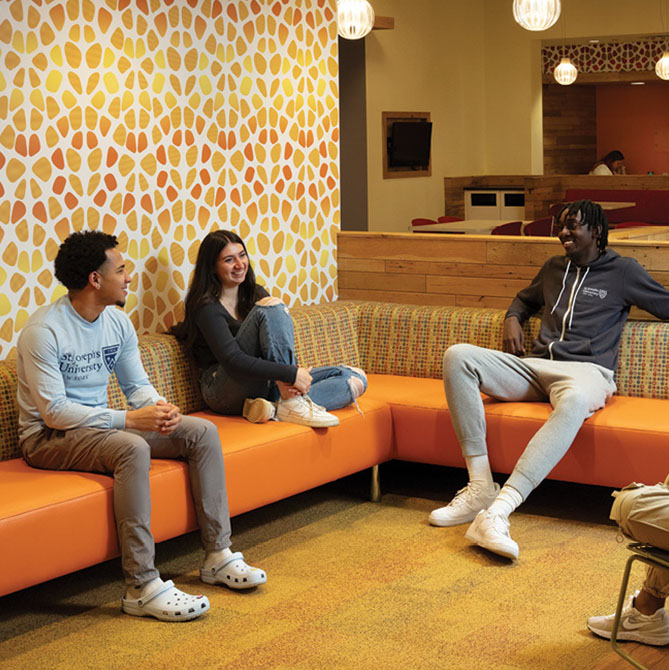Three students sitting in a lounge area on a modern orange couch with vibrant colored wallpaper behind them