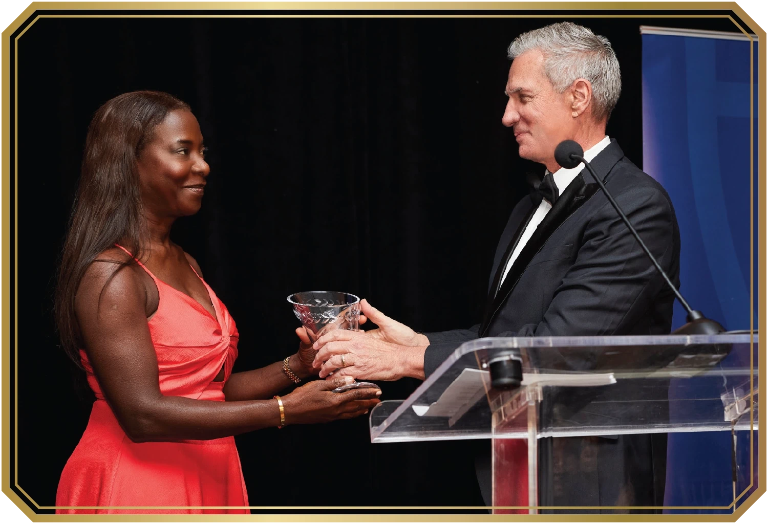 Sandra Lindsay wears a shiny coral dress while accepting her award from President Boomgaarden