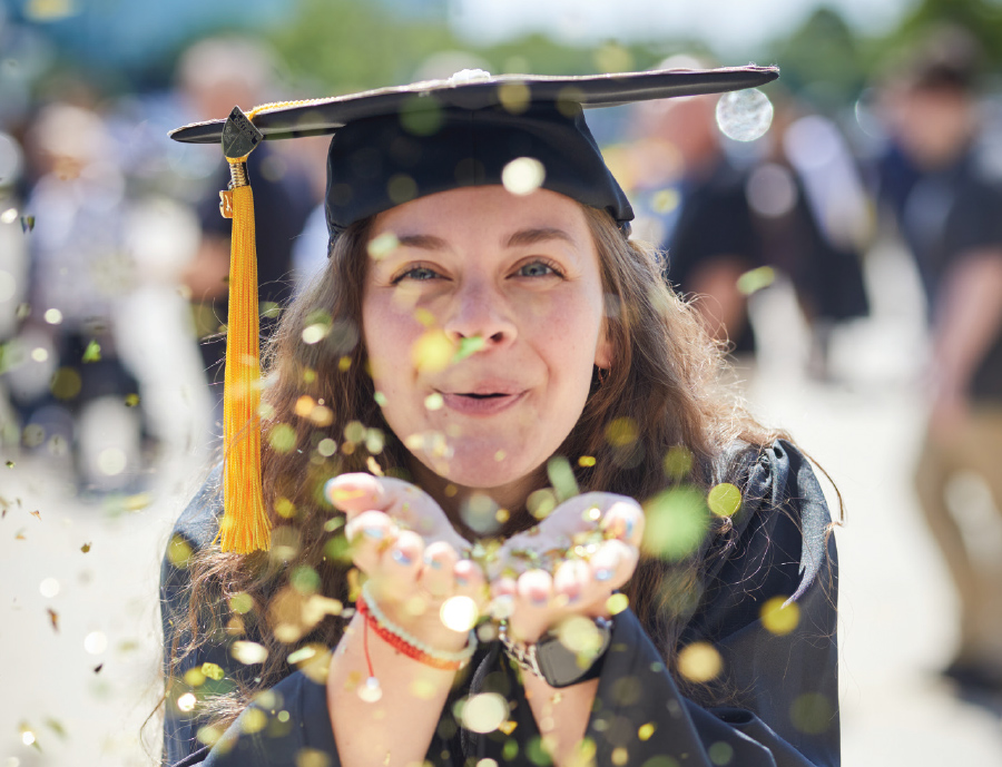 female graduate blowing confetti towards camera