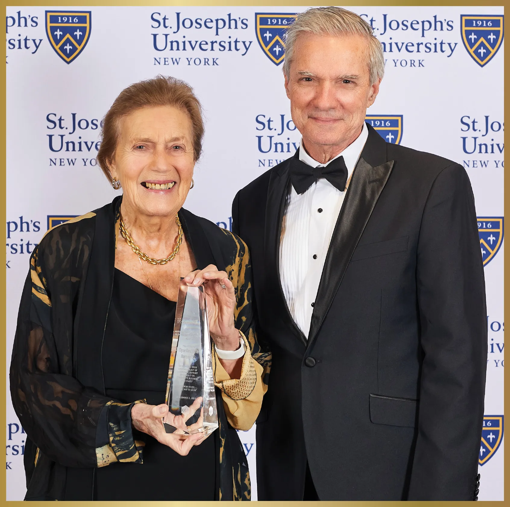 Elyse Deublein Harney ’52 smiles holding a glass award and standing beside a smiling President Boomgaarden
