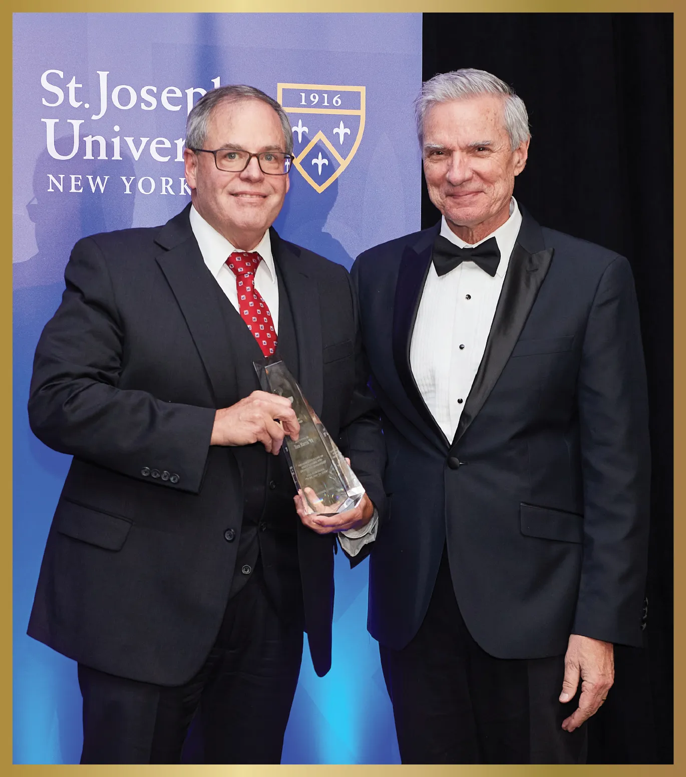 Tom Harris ’91 smiles holding a glass award and standing beside a smiling President Boomgaarden