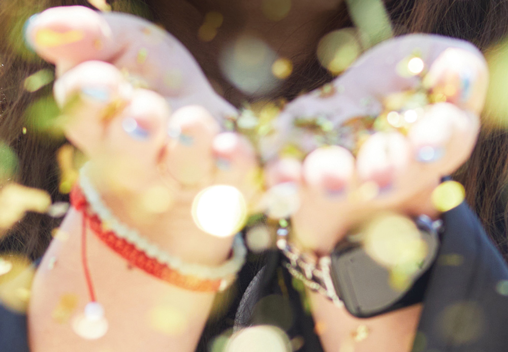 Close-up of hands holding or releasing glitter with a red bracelet and watch visible.