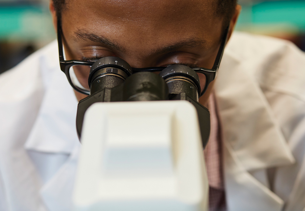 Close-up of a person in a lab coat looking through a microscope.
