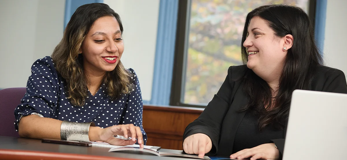 Kristen Murphy sitting at a table with another woman and pointing at a paper while smiling