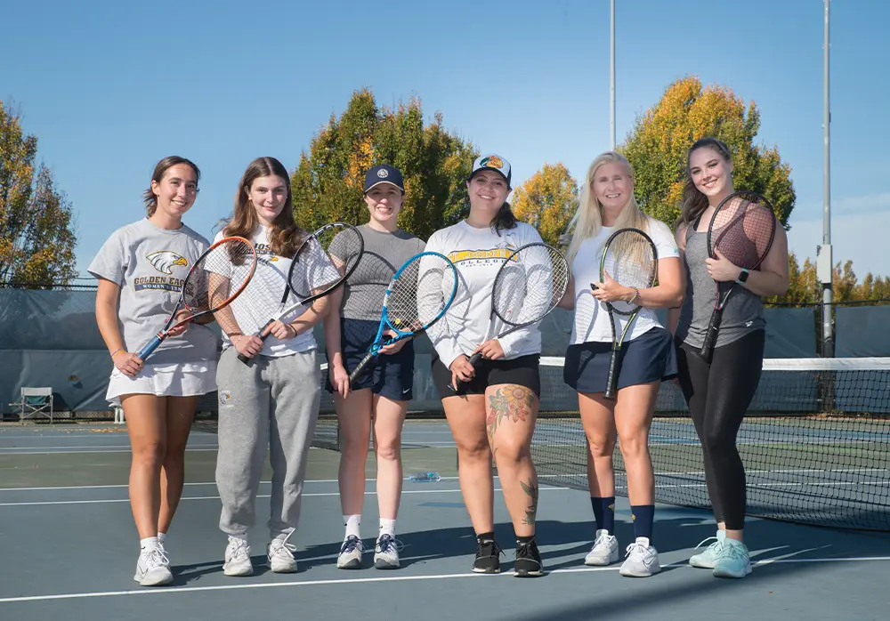 group of alumni holding tennis rackets and posing on the court