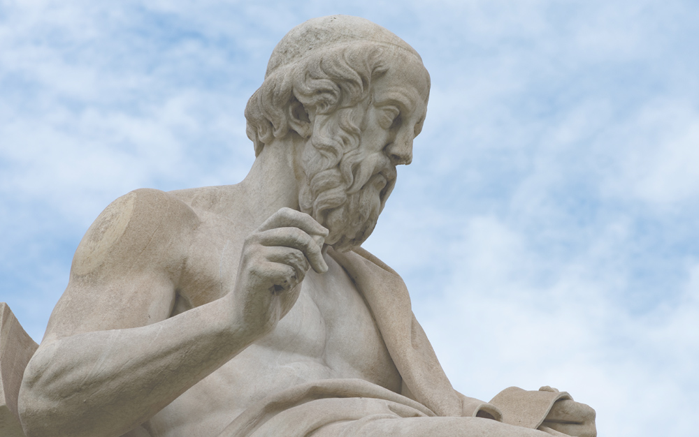 Marble statue of an elderly bearded man against a blue sky with clouds.