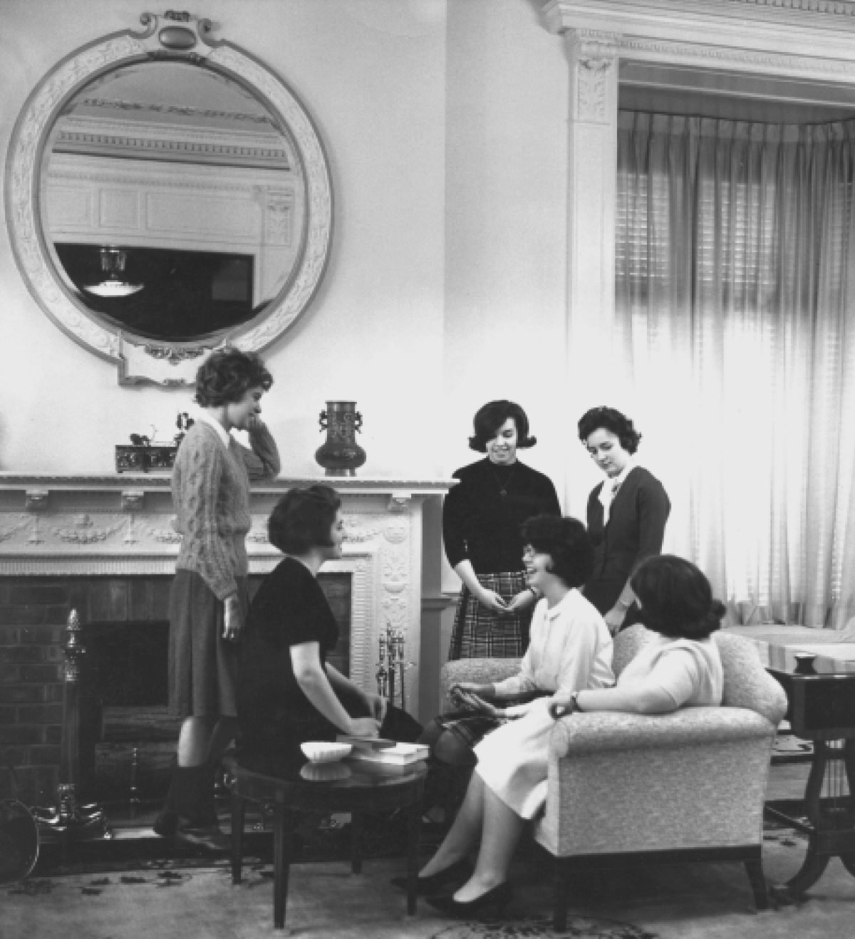 Black and white vintage retro photograph of young female St. Joseph's University New York students all situated inside conversing among each other within the Parlors in Burns Hall, which is a Georgian-style room area