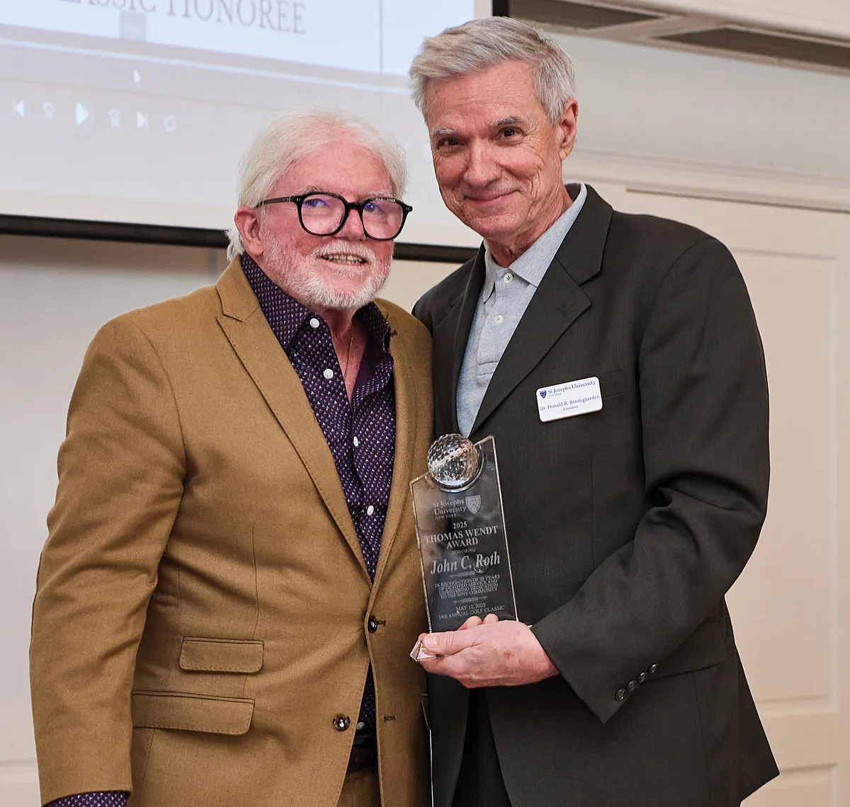 John Roth wearing a tan blazer and glasses posing with SJNY President Donald R. Boomgaarden holding a commemorative award.