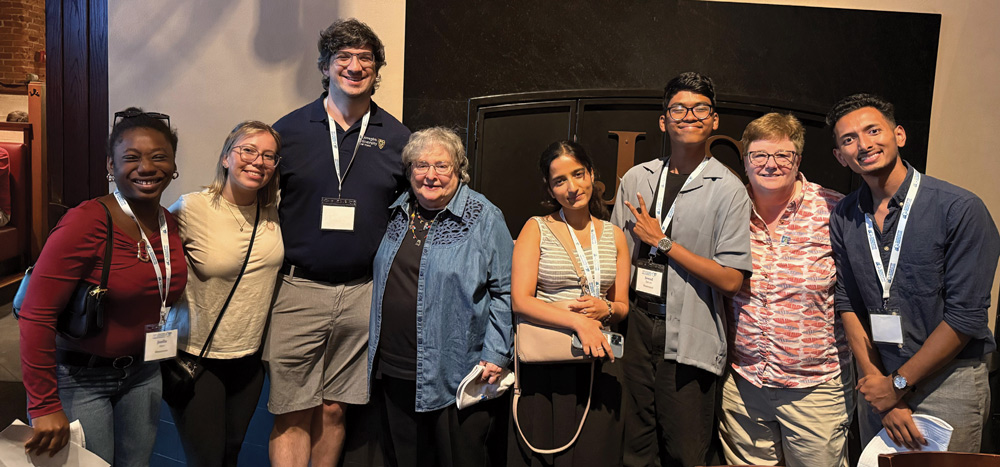 Eight people standing together indoors, smiling at the camera.