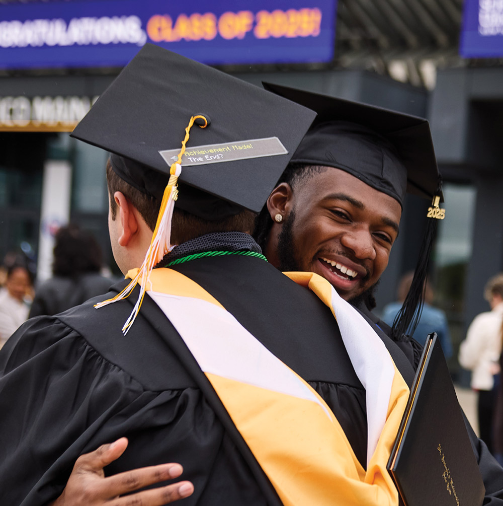 A close-up of two graduates in caps and gowns sharing a warm embrace.