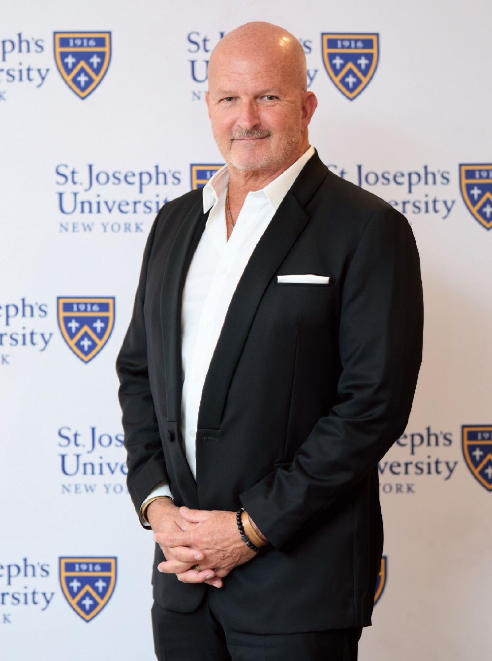 John Sparling in a black blazer and white shirt posing in front of a St. Joseph's University backdrop.
